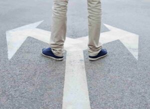 A man standing in the middle of a road with two painted arrows that point in opposite directions